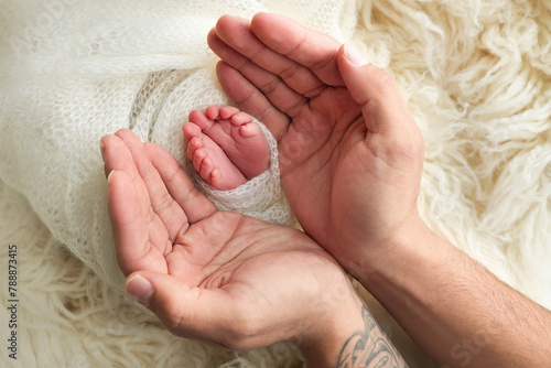 The palms of the father, the mother are holding the foot of the newborn baby in a white blanket. Feet of the newborn on the palms of the parents. Studio macro photo of a child's toes, heels and feet