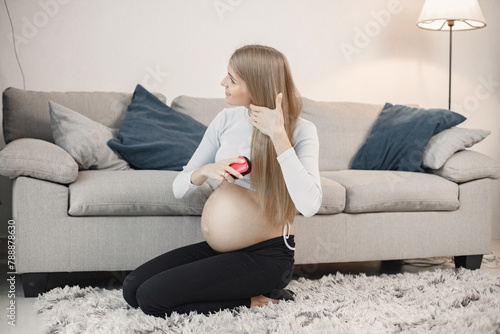 Pregnant lady sitting near a sofa in living room and brushing her hair