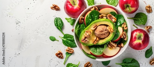 Top view of a fruit salad featuring red apples, avocado, spinach, and walnuts on a light background, with space for text. Displayed in a flat lay style.