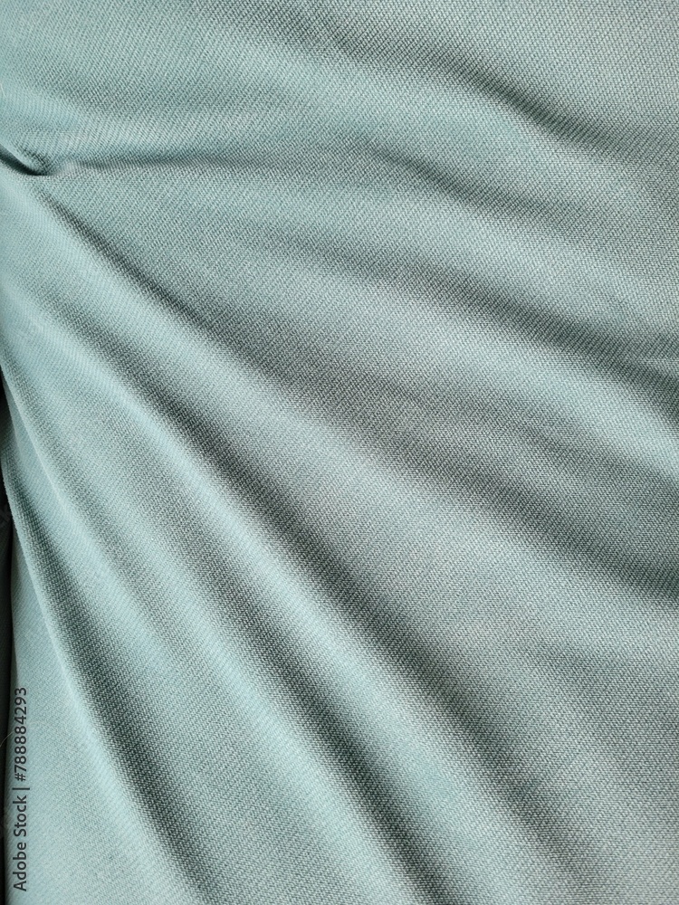 Fototapeta premium Abstract close-up of a mint-colored fabric. The folds on the fabric cast a shadow and create a volumetric background. 