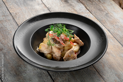 Gnocchi with chicken and garlic in cream sauce in a black plate on a wooden background, close up