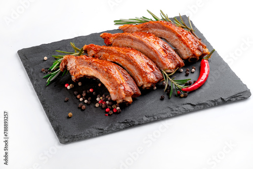 A portion of barbecue pork ribs cut into pieces in BBQ sauce on a black slate board isolated on a white background