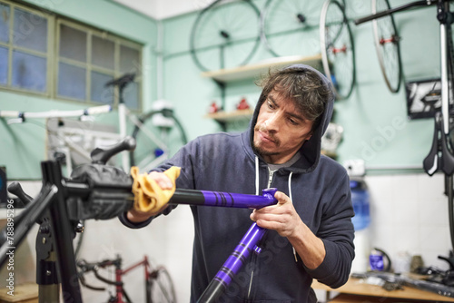 Hispanic young man working on a custom bike frame painting design in purple and black, a creative and technical handcrafted process, in his workshop.