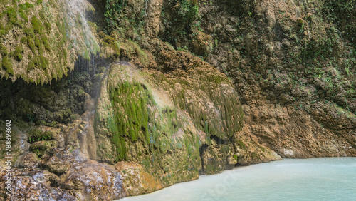 A beautiful tropical waterfall. Thin streams of water flow down the mossy stone terraces of the slopes, forming a veil. Turquoise lake at the foot of the cliff. Philippines. Cebu. Tumalog Falls.
