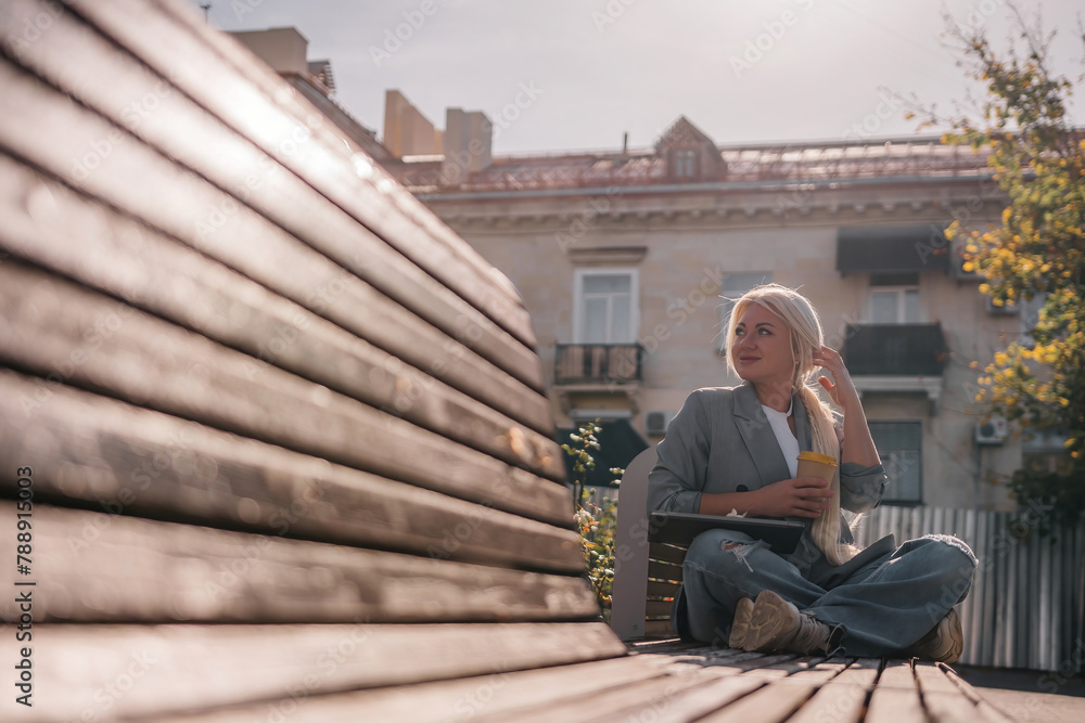 A woman sitting on a bench with a cell phone in her hand. She is wearing a suit and she is working on her phone. A woman sitting on a bench with a cell phone in her hand. She is wearing a suit and she is working on her phone.