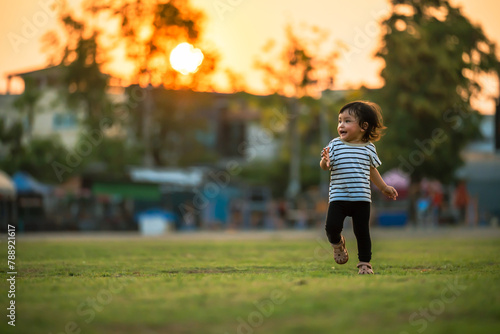 happy toddler girl running on grass field in park at sunset
