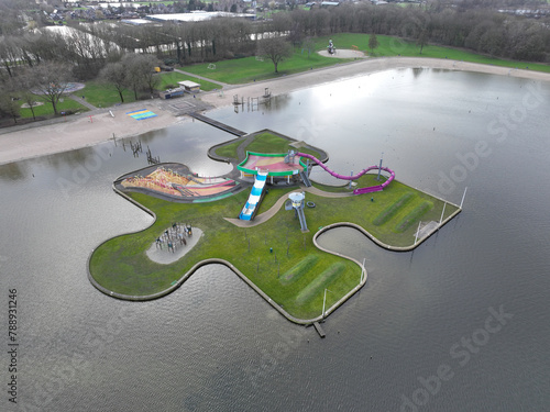 Children recreational playground, playfull colors, climbing rack, slide and other attributes on a puzzle piece on water. Aerial drone view.