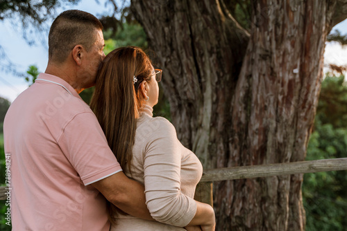 Beautiful adult couple in love talking and looking at their natural surroundings, daydreaming. Happy romantic husband and wife outdoors. Mother's day, family and father's day. Trees.