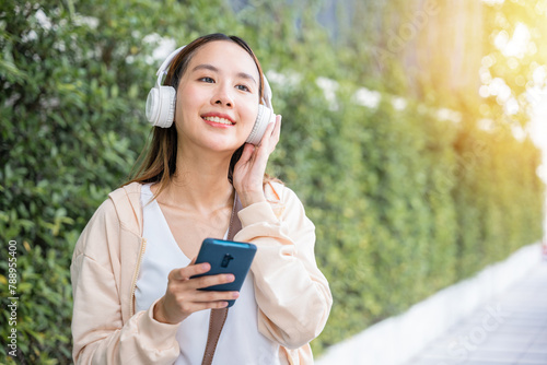 In midst of an urban city garden a happy young woman uses wireless headphones to choose and enjoy her favorite music dancing with pure joy. Her carefree spirit is a beautiful reflection of season. photo