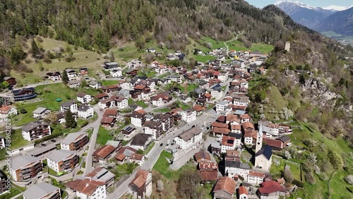 Quaint small town in Switzerland mountain slope during sunny day. Church and historic buildings in city. Aerial top down circling shot.