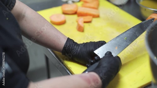 Chef wearing black sterilized gloves slicing squash with a sharp knife on a wide yellow cutting board; food preparation; preparing to cook; vegetable ingredients photo