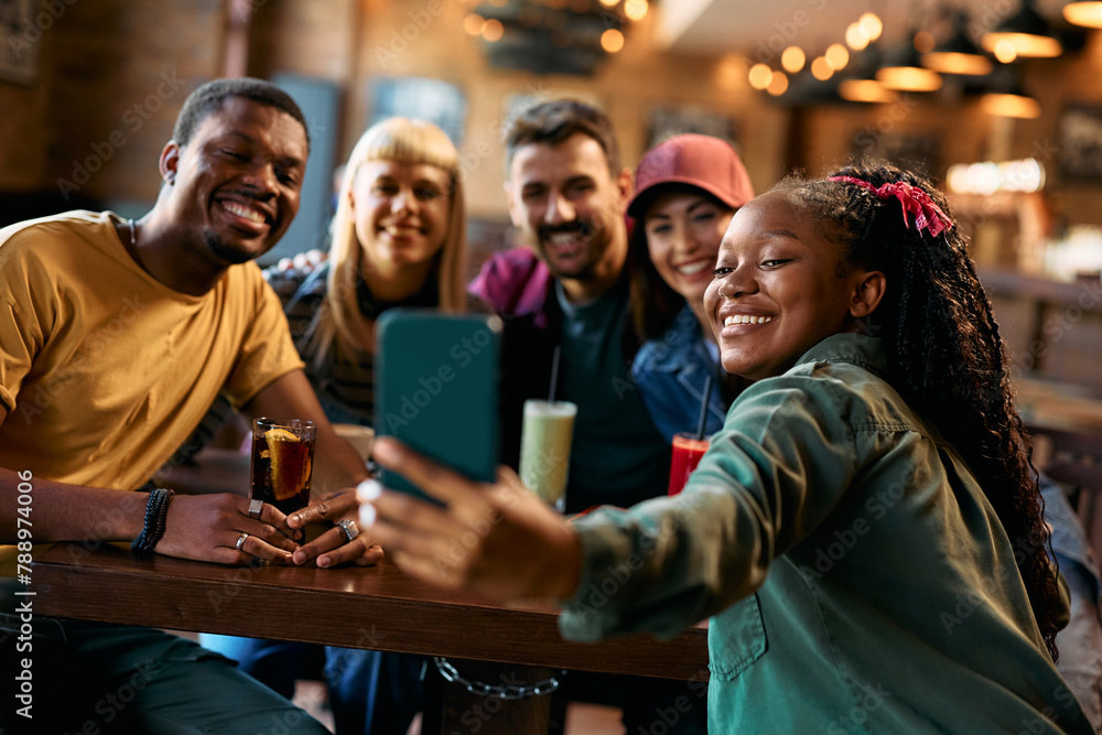 Obraz premium Happy black woman taking selfie with her friends in bar.