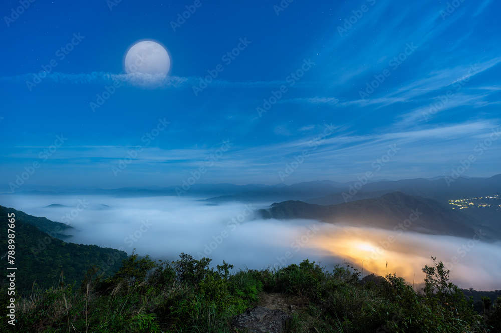 The quiet sea of ​​clouds and blue moon give people a mysterious feeling. View of the mountains surrounding Emerald Reservoir. Xindian District, Taiwan.