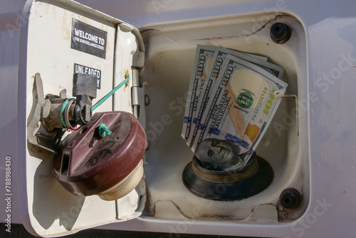 American or US Dollars fitted into a fuel filler or gas hole of a car's fuel tank, symbolizing the increase of the price of fuel, petrol, diesel or gas.