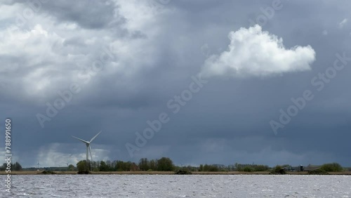 Single windmill on the edge of a lake rotating in storm wind against ominous, dark stom sky, regenerating renewable, sustainable green energy and electricity photo