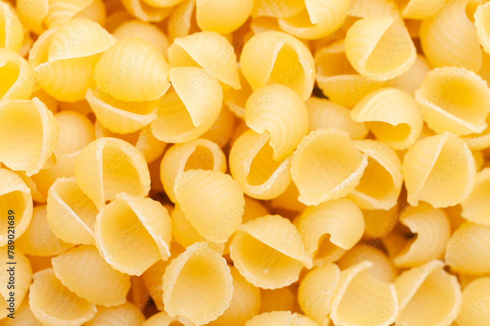 Uncooked, yellow, small shell shaped pasta background. Top view. Close-up Uncooked, yellow, small shell shaped pasta background. Top view. Close-up
