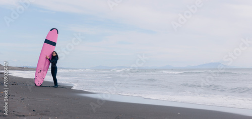 Extreme surfer woman in wetsuit with surfboard go to winter surfing in Atlantic ocean Kamchatka Russia. Banner Adventure travel sport concept