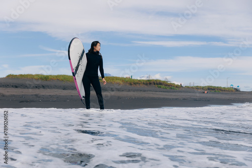 Happy surfer woman in wetsuit with surfboard go to winter surfing in ocean. Adventure Extreme travel sport concept