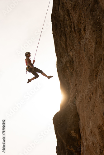 A person is climbing a rock wall with a rope. The person is wearing a red shirt and is in the air