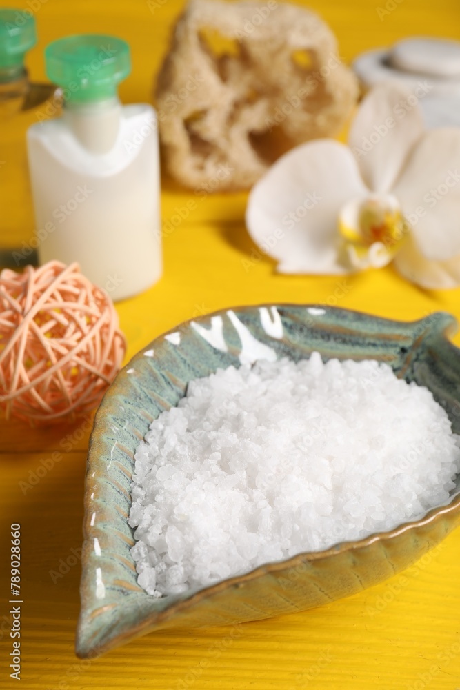 Natural sea salt in bowl and other spa products on yellow wooden table, closeup Natural sea salt in bowl and other spa products on yellow wooden table, closeup