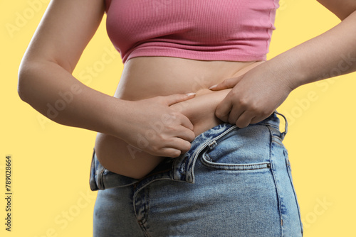 Woman touching belly fat on yellow background, closeup. Overweight problem © New Africa