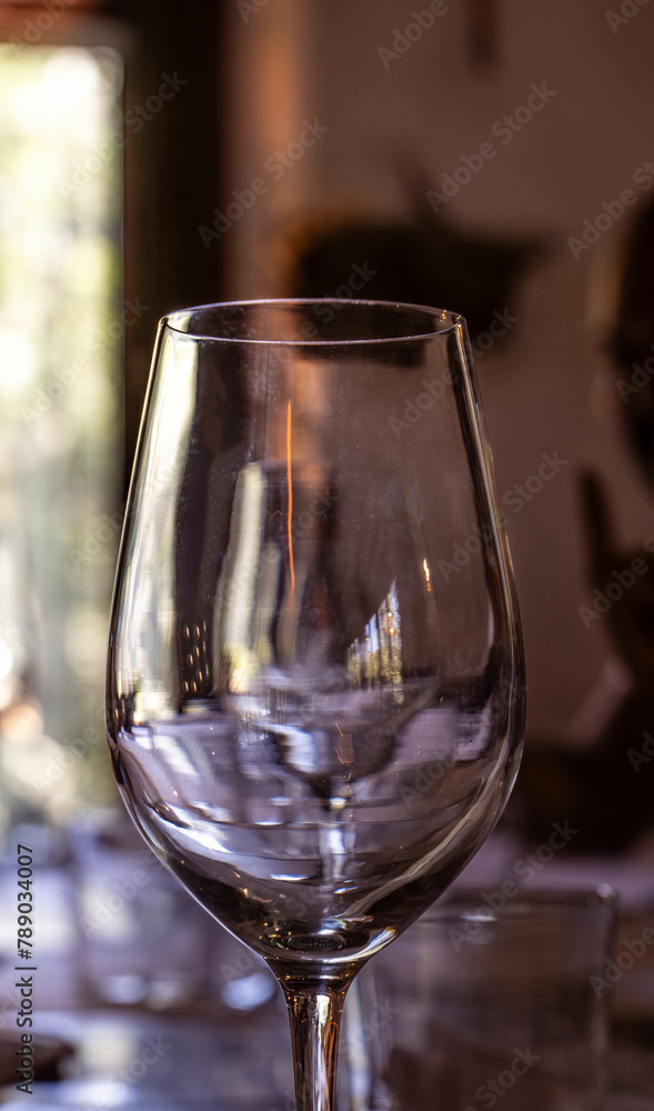 Close-up of glass wine glass illuminated by evening light reflecting a window overlooking a forest of a rustic restaurant of a mountain hotel for a romantic date. Close-up of glass wine glass illuminated by evening light reflecting a window overlooking a forest of a rustic restaurant of a mountain hotel for a romantic date.