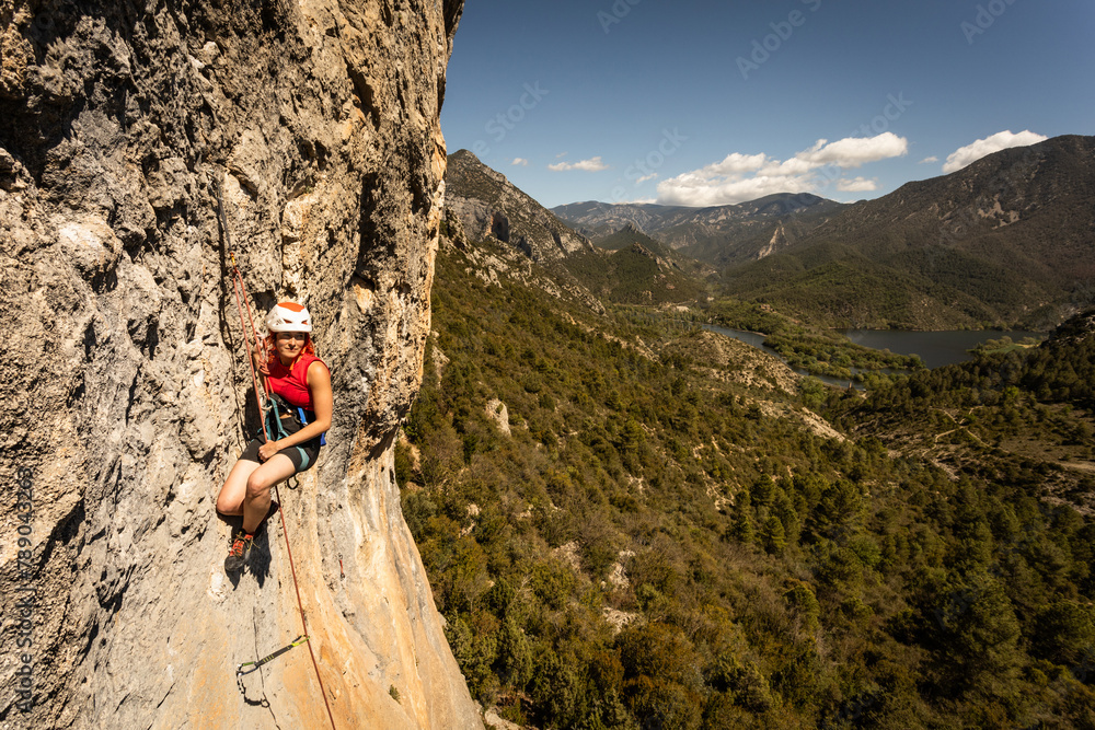 A woman is climbing a rock wall with a red jacket - obrazy, fototapety, plakaty 