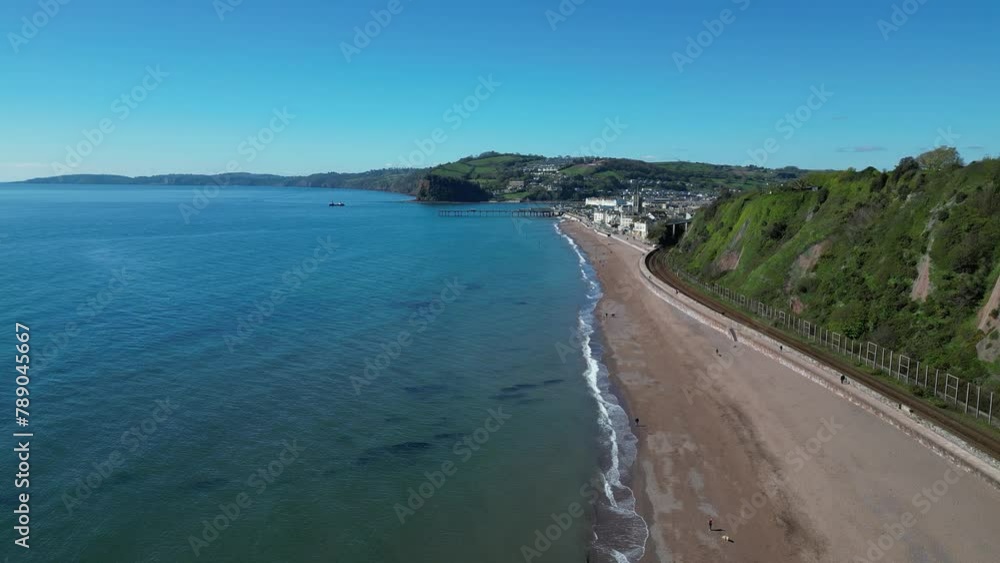 Teignmouth, South Devon, England: DRONE VIEWS: The drone flies over the shore towards the Grand Pier and town to the right. Teignmouth is both a port town and a popular English tourist destination. Teignmouth, South Devon, England: DRONE VIEWS: The drone flies over the shore towards the Grand Pier and town to the right. Teignmouth is both a port town and a popular English tourist destination.