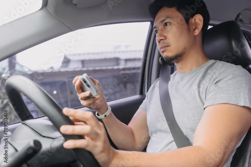 Side view of asian man using mobile phone inside the car while driving on road, incautious, accident cause. photo