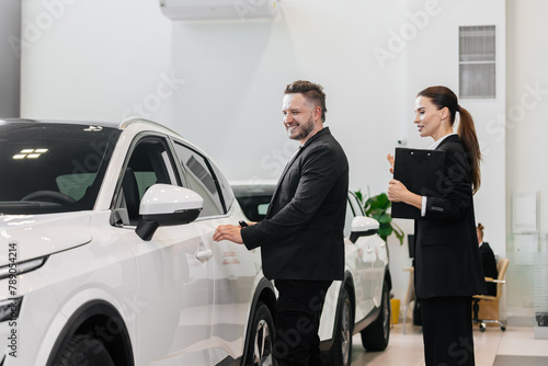 An interested buyer consults with a car dealership manager about the models and characteristics of a modern electric car. Concept of buying and selling a car, deal.