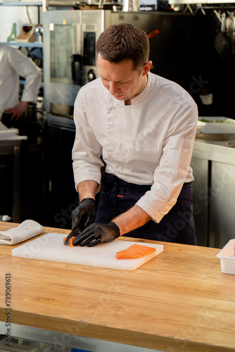 chef in a white jacket in the kitchen with black gloves cuts salmon fillet on white board