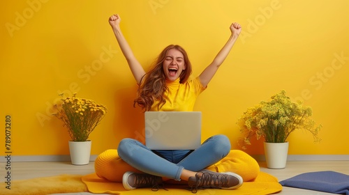 A young woman is sitting on the floor in front of a laptop, with her arms in the air and a surprised expression on her face. photo