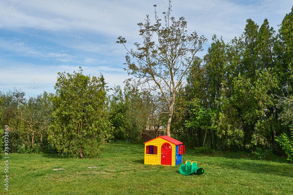 Charming countryside scene with little and vibrant plastic swing set and quaint cottage amidst lush fields