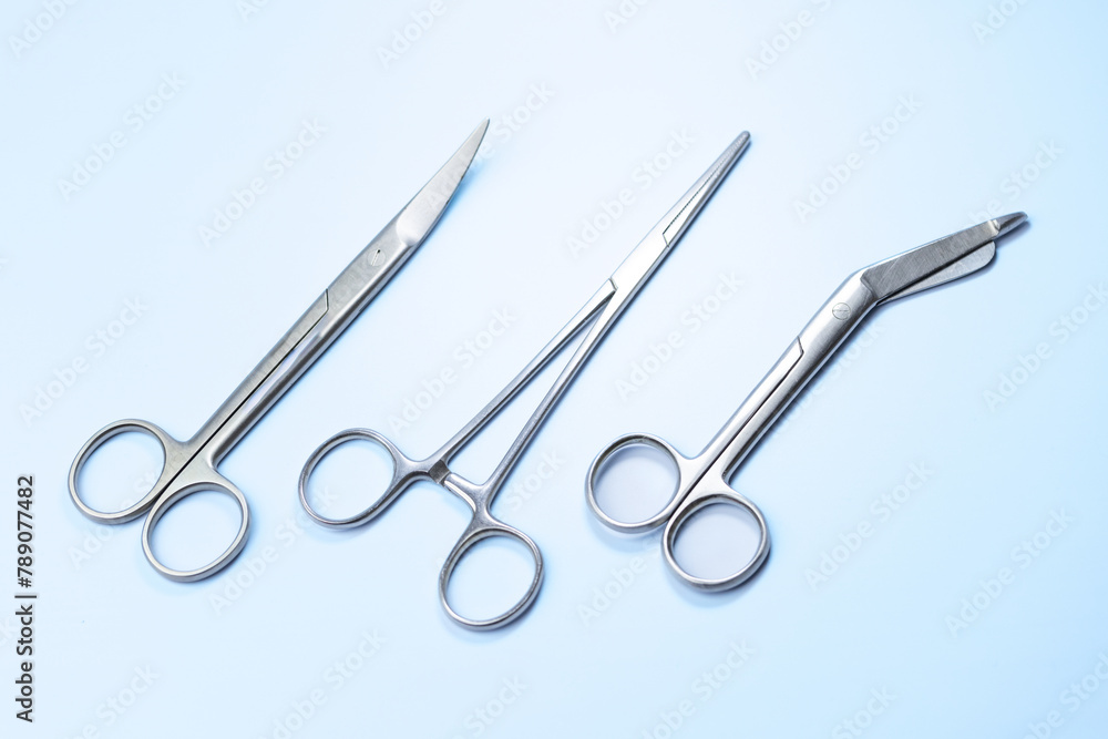 Three pairs of surgical scissors are shown on a blue background. The scissors are all silver and appear to be of the same size Three pairs of surgical scissors are shown on a blue background. The scissors are all silver and appear to be of the same size