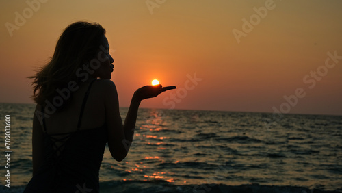 The silhouette of a woman, her figure cast in shadow, as if she is blowing the sun away from her palm.