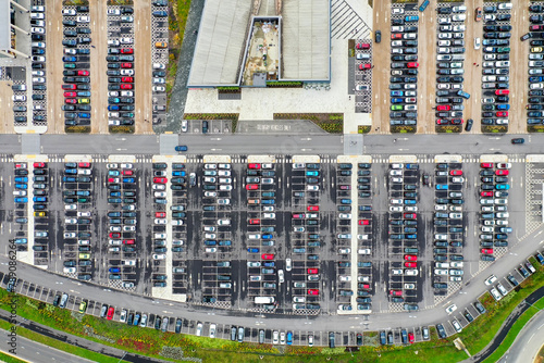 Aerial top view of a busy carpark showing all different kinds of cars parked up and driving on the road looking for a space.