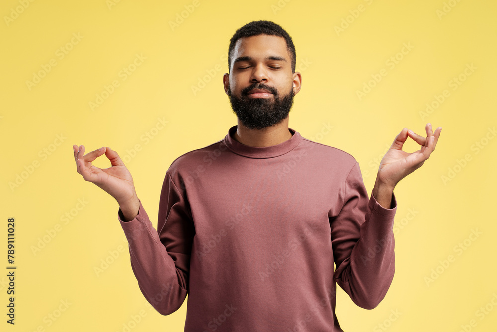 African American man relaxing with eyes closed, doing meditation gesture, over yellow background African American man relaxing with eyes closed, doing meditation gesture, over yellow background