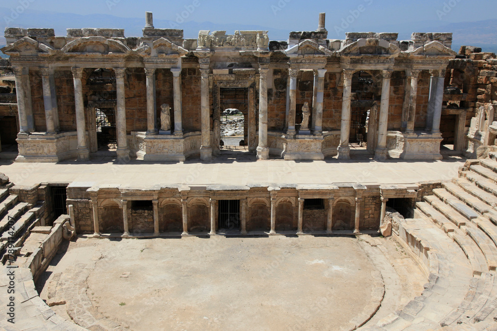 Fototapeta premium Ancient antique amphitheater, columns on the stage of the amphitheater, steps and antique statues with columns in the amphitheater, Hierapolis in Pamukkale, Denizli City, Turkey.