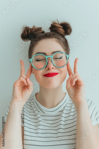 A youthful female with a playful expression  wearing large teal glasses  poses with a peace sign.