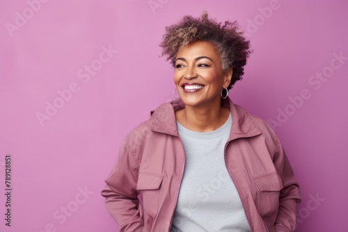 Portrait of a happy afro-american woman in her 50s wearing a trendy bomber jacket in front of solid pastel color wall