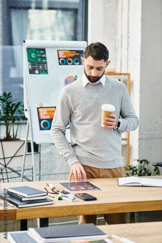 A man relaxes at a table with a cup of coffee in a bustling office environment, taking a moment to regroup amidst corporate hustle. photo