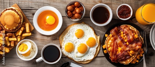 Top view of a wooden surface displaying a complete American breakfast, with fried eggs, bacon, hash browns, pancakes, orange juice, and coffee.