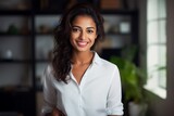 Portrait of a cheerful indian woman in her 20s wearing a classic white shirt isolated on stylized simple home office background