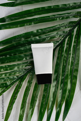 Plastic tube for cream or lotion. Skin care or sunscreen cosmetic with stylish props on tropical monstera leaves background