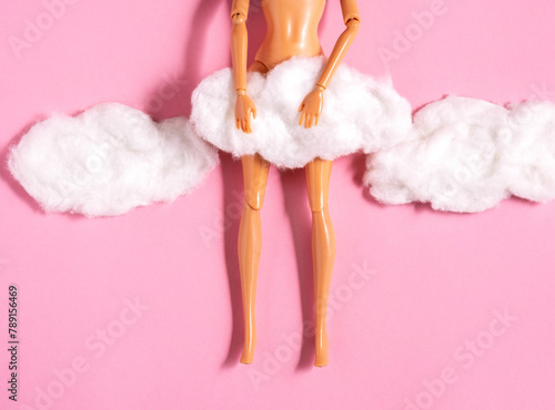 Plastic doll legs with cotton wool clouds covered crotch on pastel pink background.