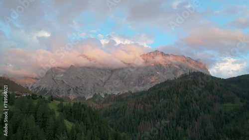 An evening aerial footage of the Sas dles Nü (Cima Nove) mountain covered in beautiful clouds. The drone is flying slowly forward above the valley in La Val village. South Tyrol, Italy. LuPa Creative.