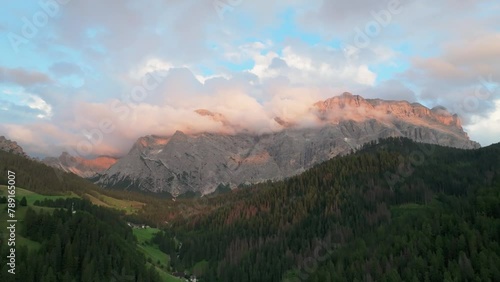 An evening aerial orbit view of the Sas dles Nü (Cima Nove) mountain covered in beautiful clouds. The drone is flying to the left above the valley in La Val village. South Tyrol, Italy. LuPa Creative. photo