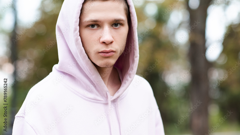Serious teenage boy 18-19 year old wearing hood and pink hoodie outdoor close up. Looking at camera. Serious teenage boy 18-19 year old wearing hood and pink hoodie outdoor close up. Looking at camera.