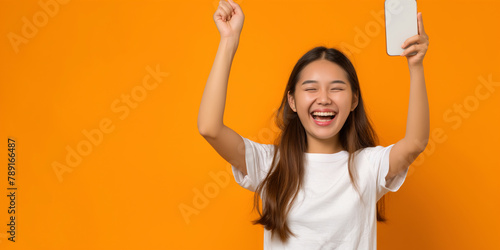 full length Happy Asian woman holding a smartphone and winning the prize on orange color background,High resolution professional photography