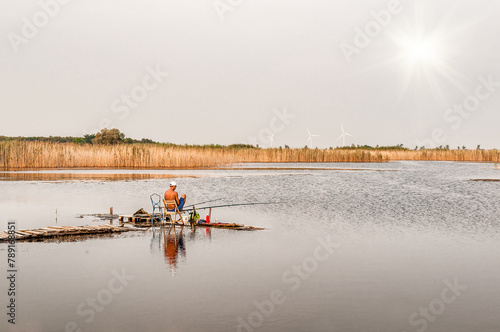 Tanned fisherman fishing with net and rod sitting on the wooden pier on lake